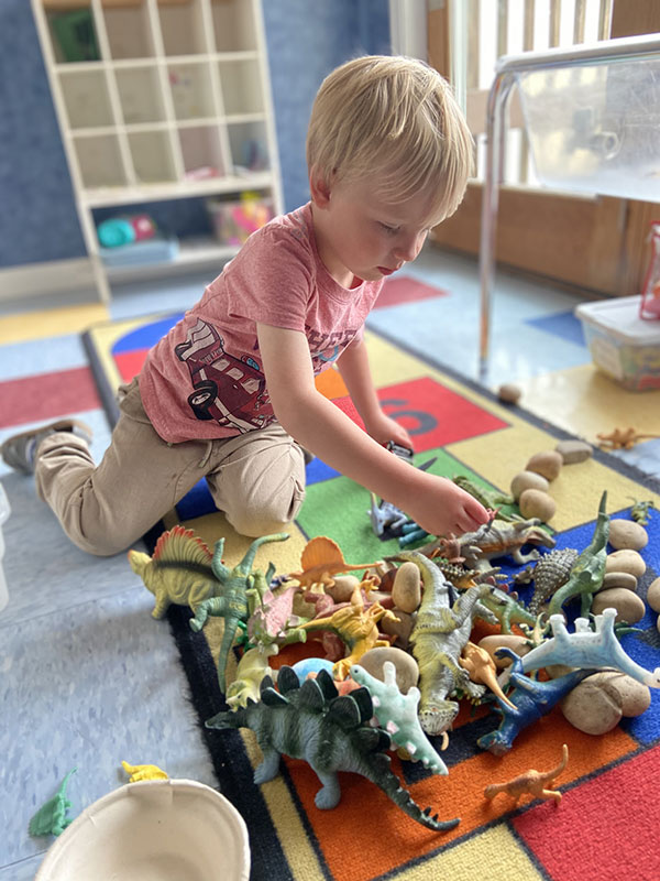 Child playing with a collection of toy dinosaurs inside the Discovery School.