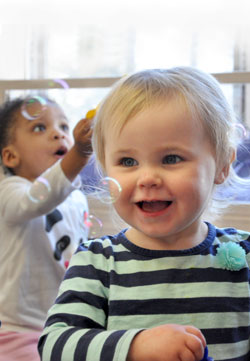 Toddler smiling at blown bubbles inside the Gigueres Discovery School.